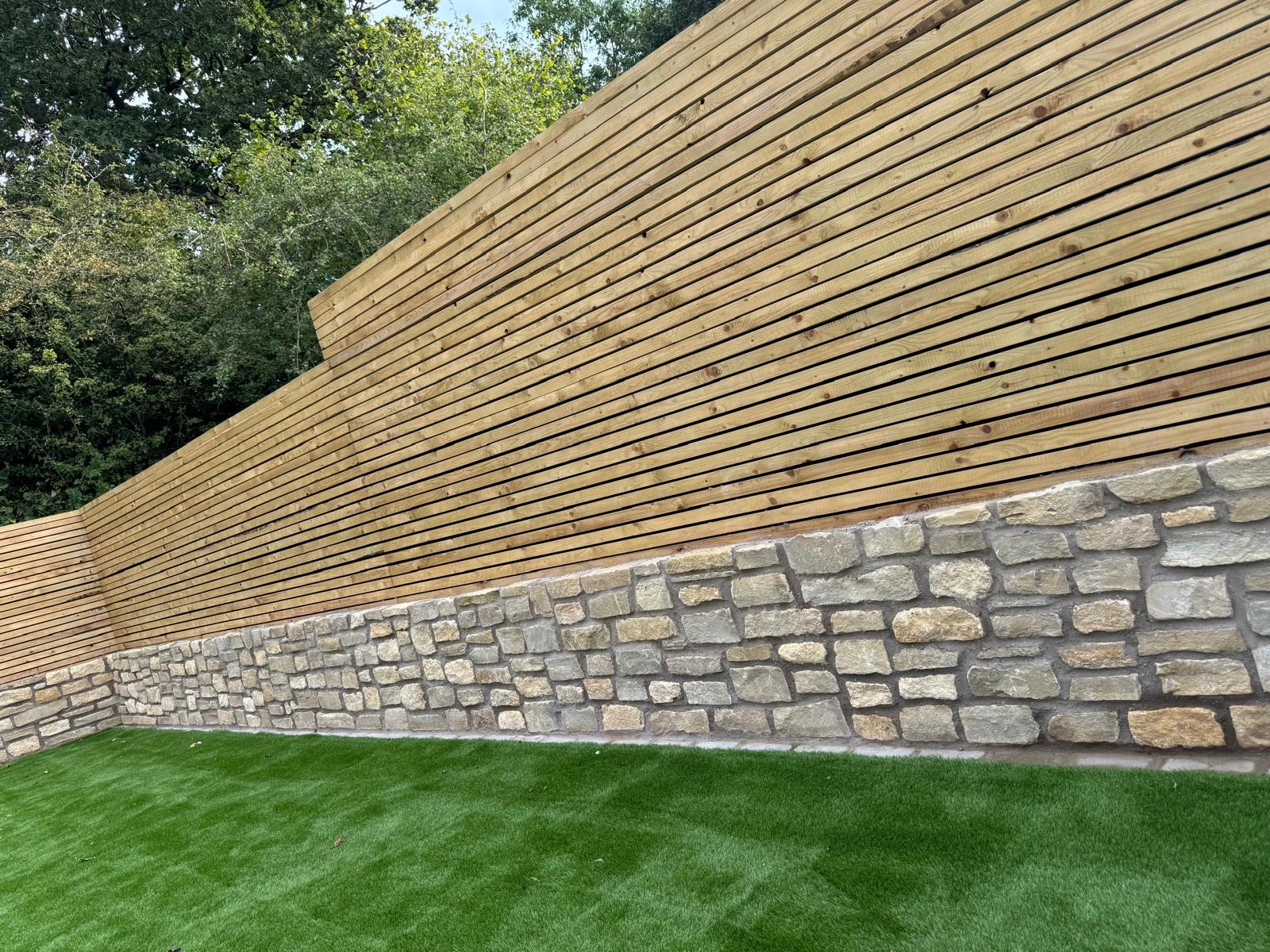 Slatted timber fence installed above a natural stone retaining wall beside an artificial lawn
