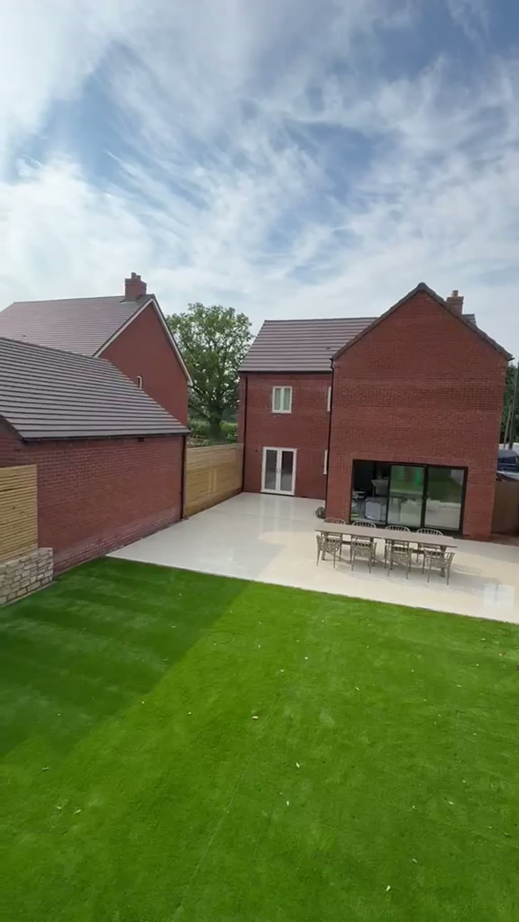 Walkthrough of an artificial grass lawn beside a cobbled seating area and slatted fencing