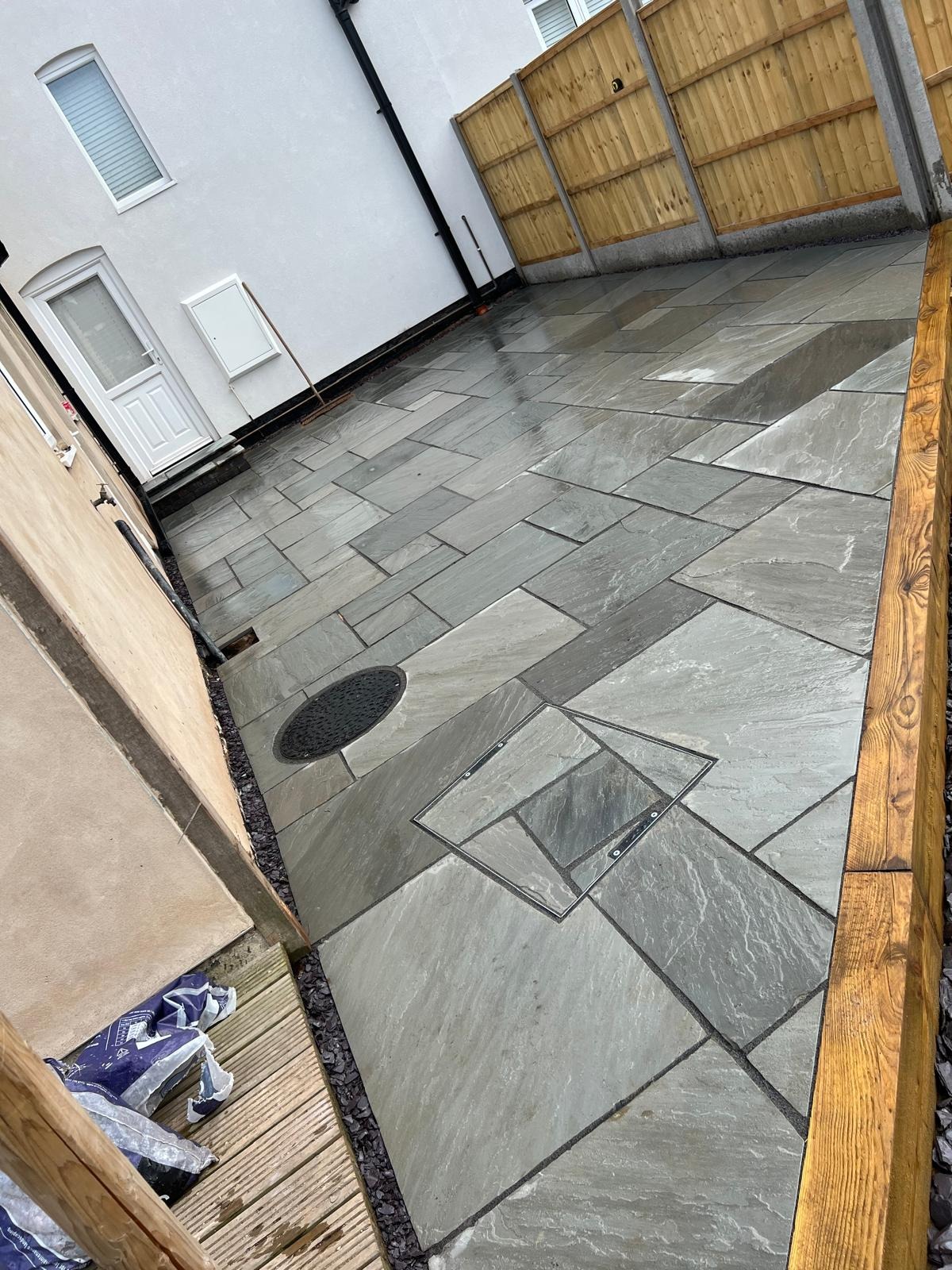 Indian sandstone patio in a random pattern with recessed manhole covers neatly cut in