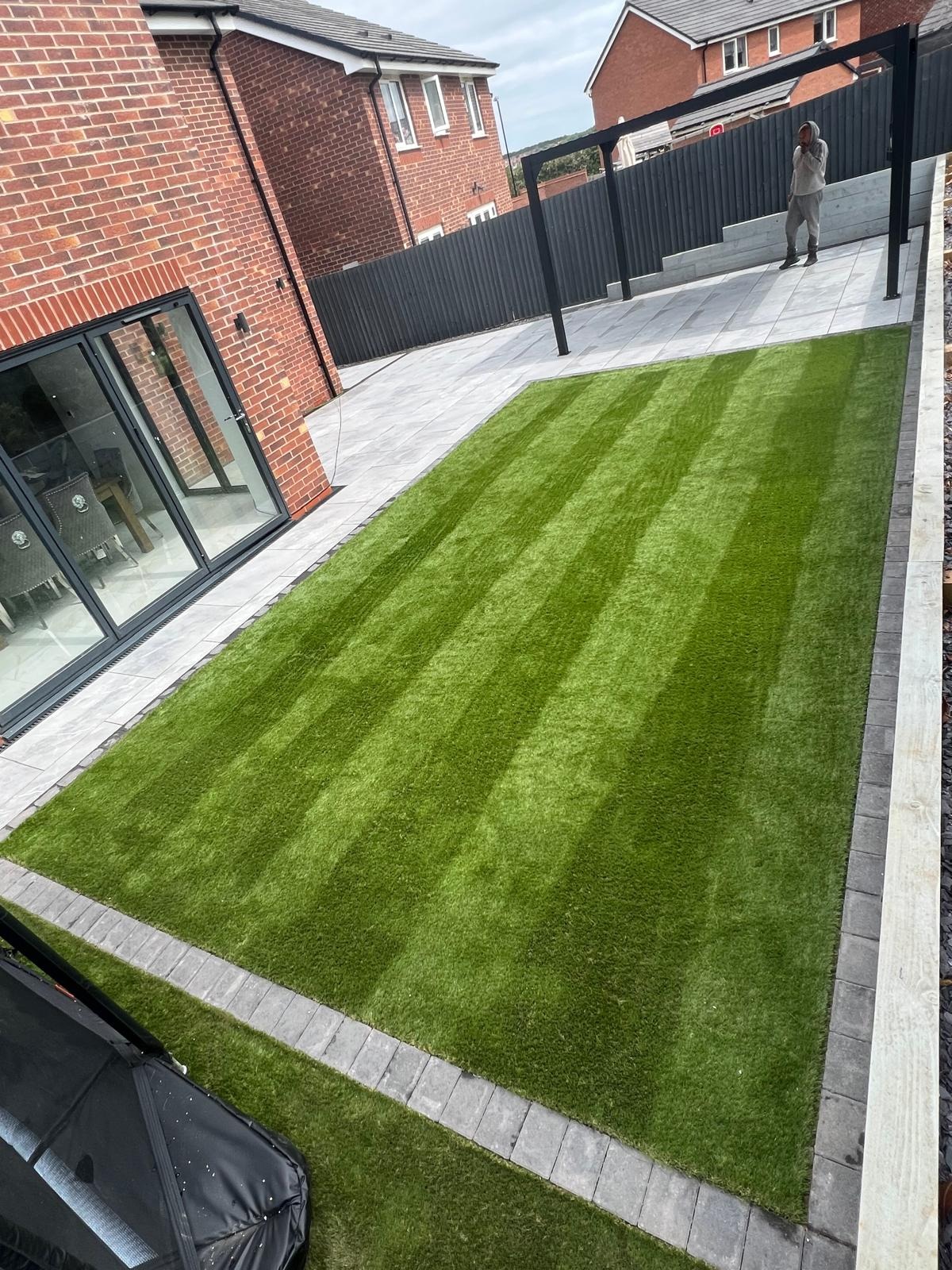 Artificial lawn and light paving laid to a crisp edge behind a brick house