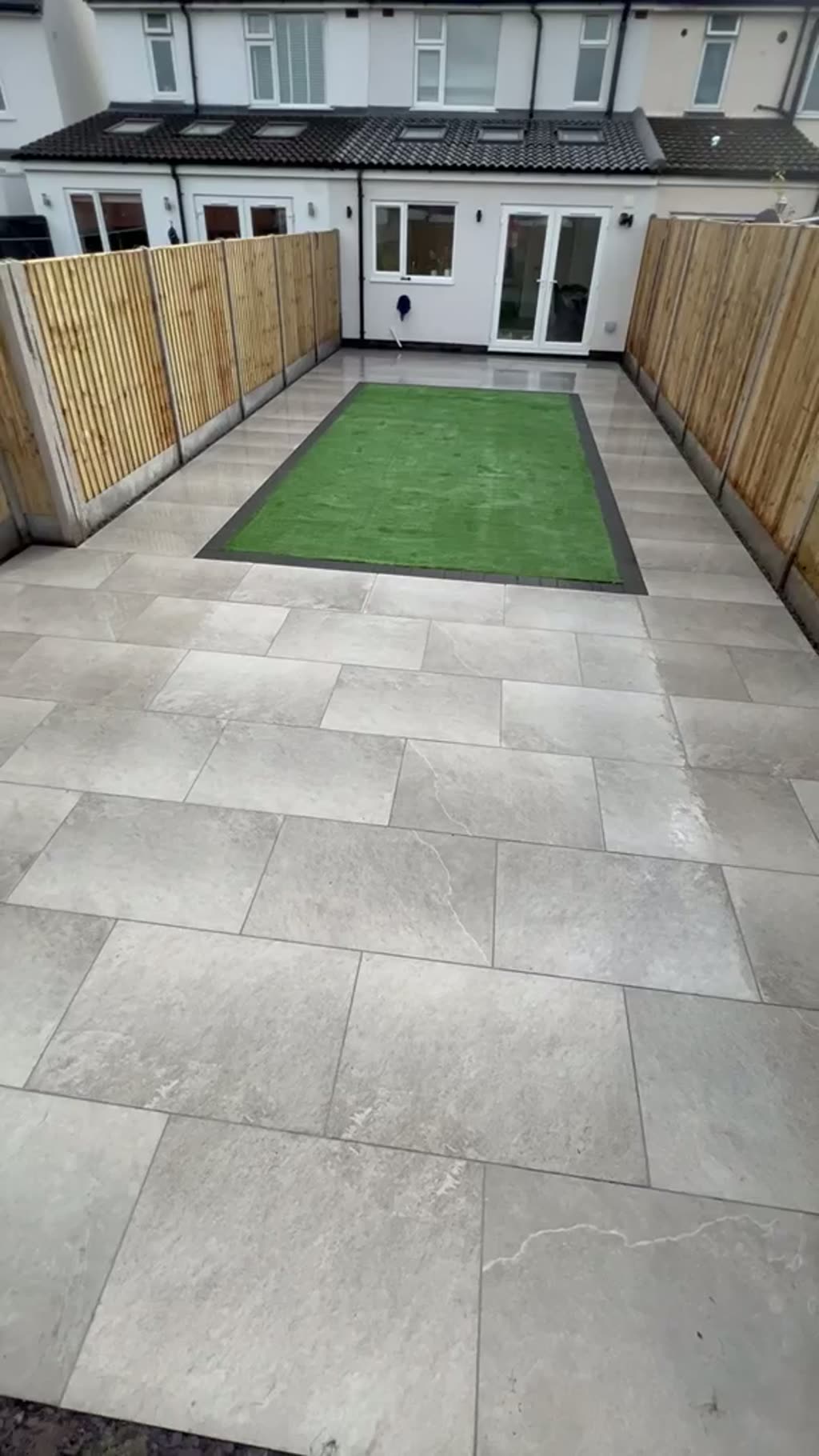 Walkthrough of a grey porcelain patio with a new close-board fence and small lawn