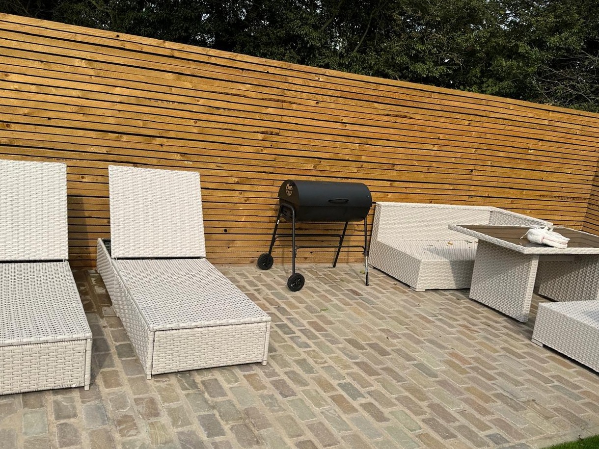 Cobblestones by SOS Landscaping: Cobblestone patio laid in tight courses with a slatted timber privacy screen and garden furniture