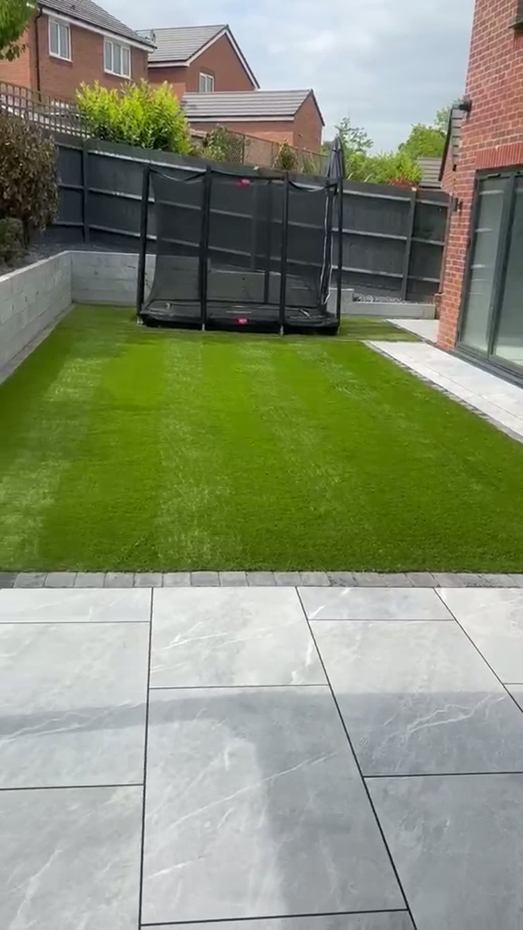Walkthrough of a porcelain paved path with slate border leading to a pergola seating area